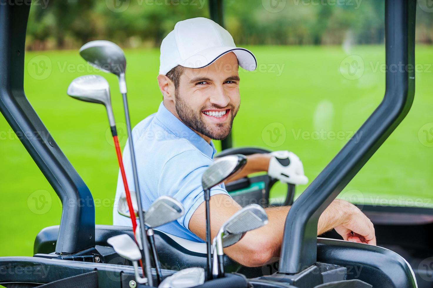 Golfer im Golfwagen. Rückansicht des jungen glücklichen männlichen Golfers, der einen Golfwagen fährt und über die Schulter schaut foto