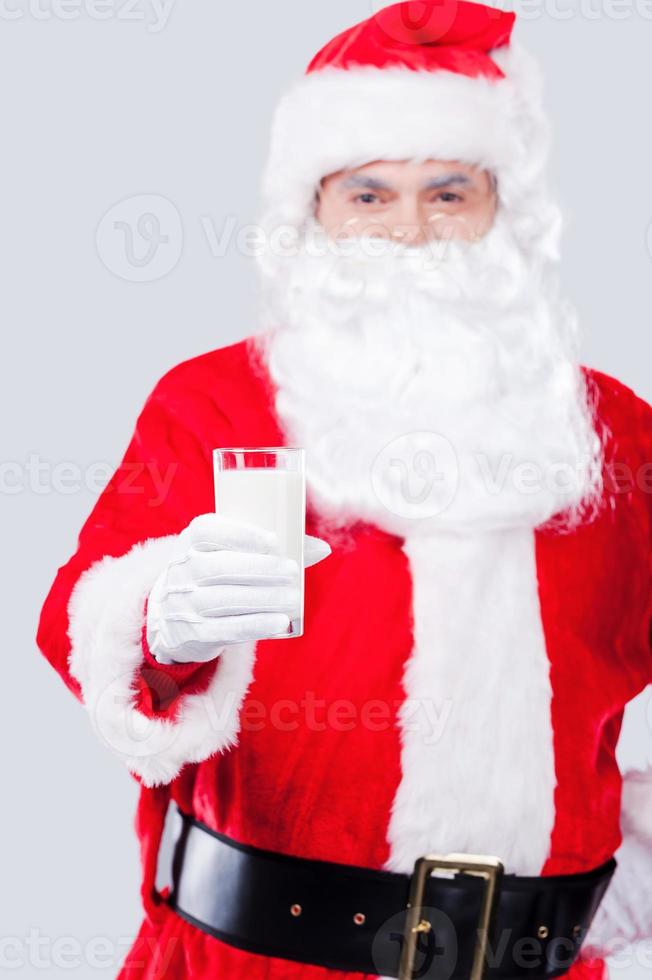 trinken sie frische milch traditioneller weihnachtsmann, der die hand mit einem glas milch ausstreckt, während er vor grauem hintergrund steht foto