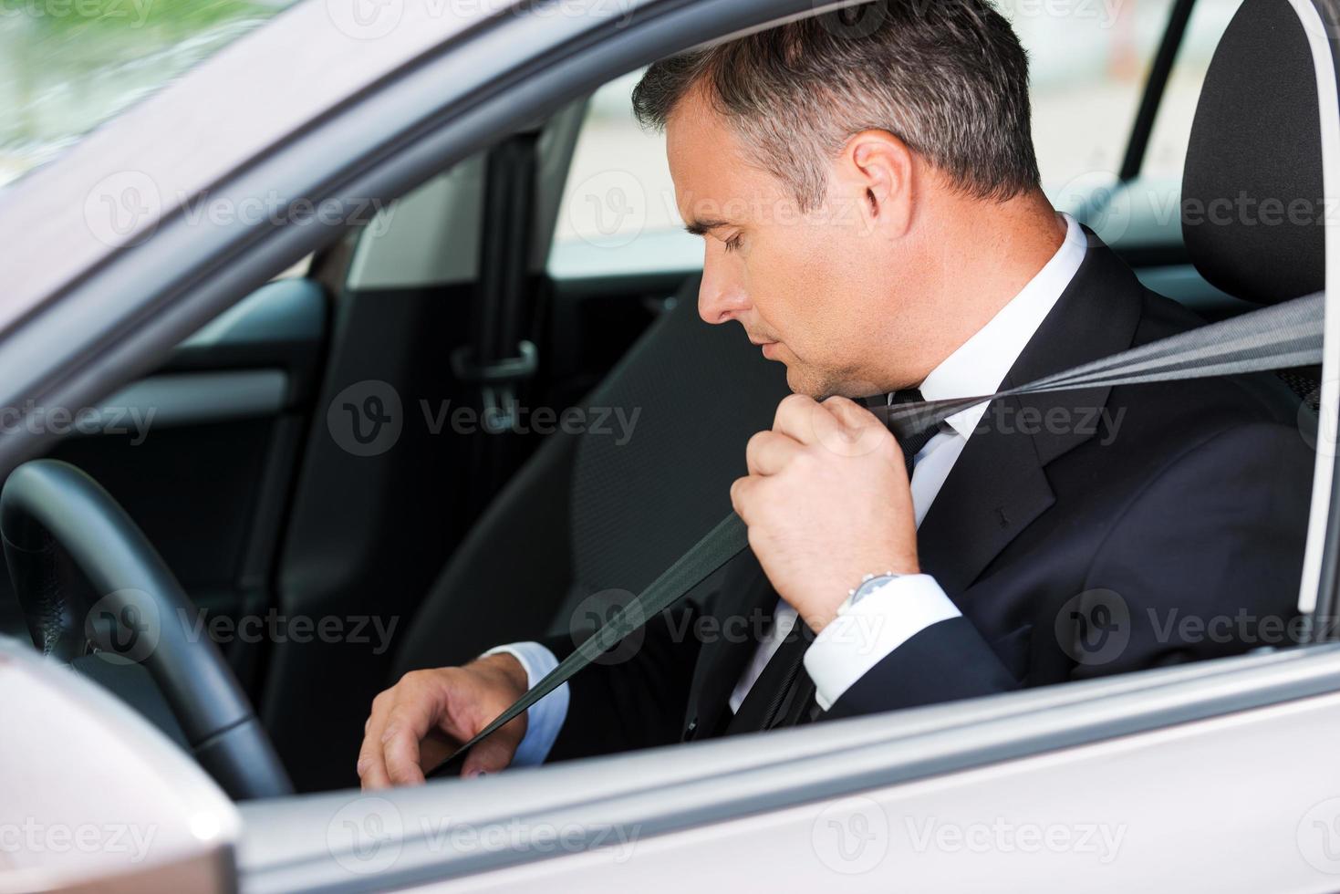 sicheres Gefühl im neuen Auto. Selbstbewusster, reifer Geschäftsmann, der den Sicherheitsgurt anlegt, während er in seinem Auto sitzt foto