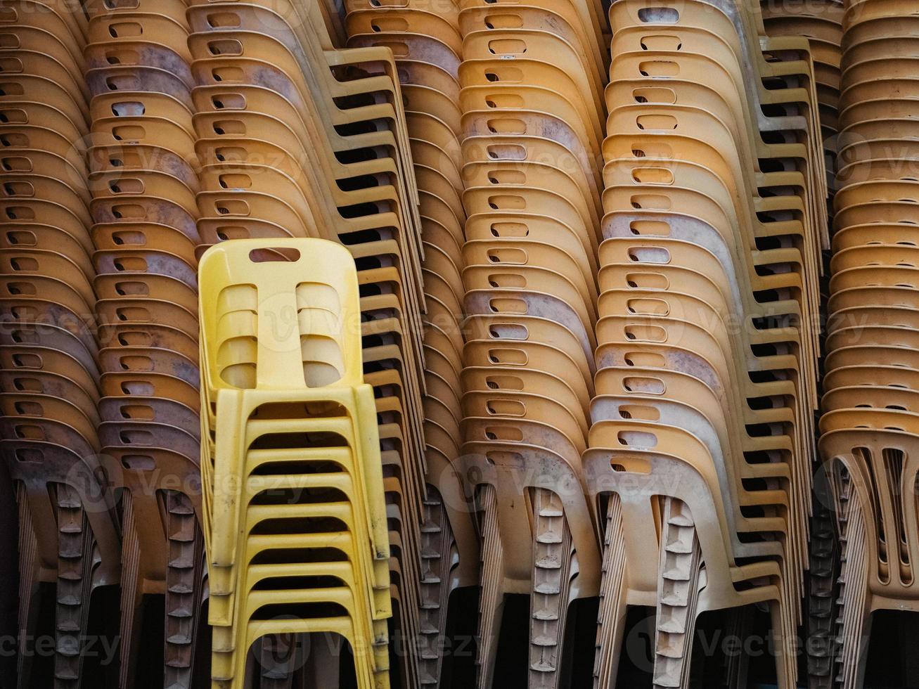 Neue und alte gelbe Plastikstühle stapeln sich hoch in einem Restaurant foto