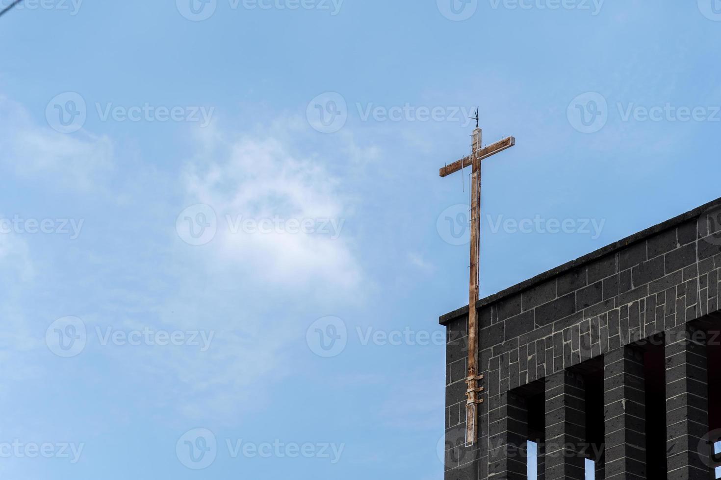 Spitze einer Kirche mit einem rostigen Metallkreuz, die Kirche ist aus Stein mit klarem blauem Himmel. Mexiko foto