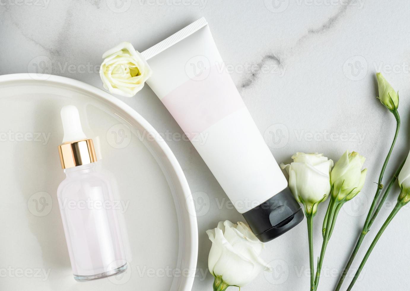 Kosmetik-Set aus rosafarbenem Schönheits-Gesichtsöl in Tropfflasche und Tube ohne Markenzeichen mit Creme oder Maske auf Marmortisch mit Eustoma-Blumen. trendiges Flat-Lay-Stillife foto