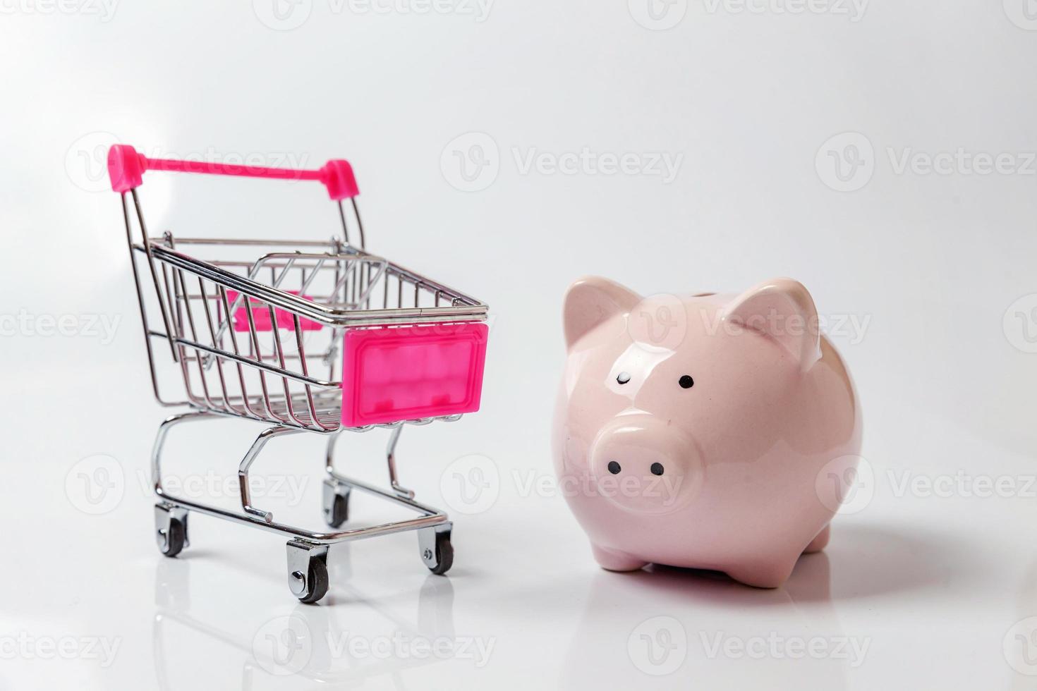 kleiner Supermarkt Lebensmitteleinkaufswagen zum Einkaufen mit Sparschwein isoliert auf weißem Hintergrund. verkauf kaufen einkaufszentrum markt shop verbraucherspar- und budgetkonzept. Platz kopieren. foto