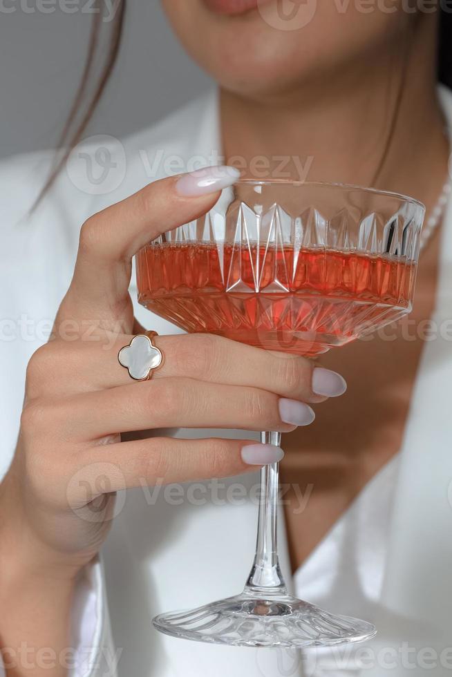 eine vertikale Aufnahme einer kaukasischen Frau, die ein Cocktailglas mit einem Ring am Finger hält foto