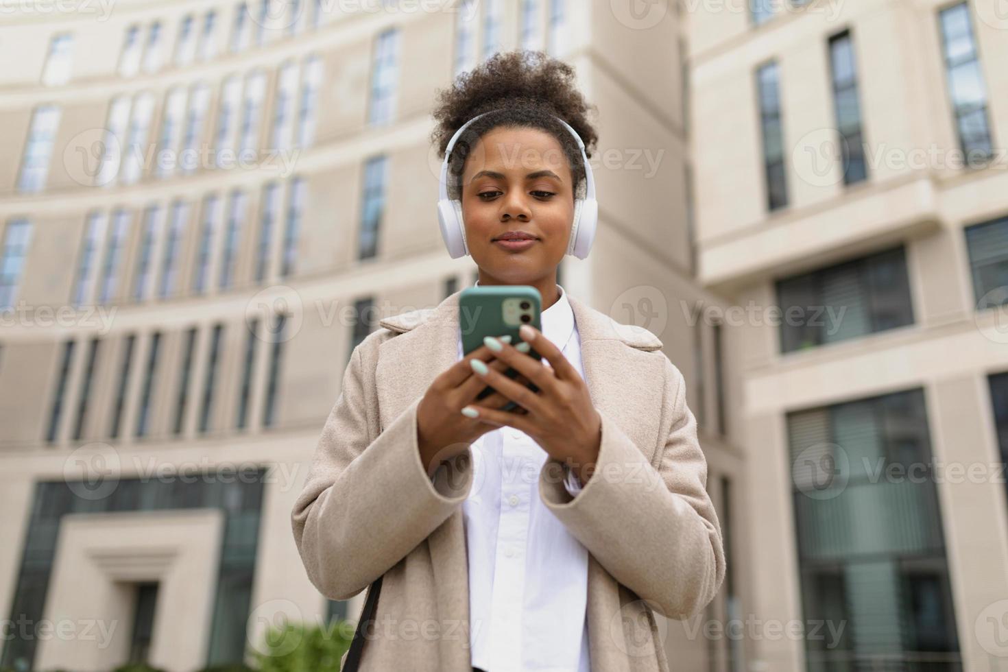 Afroamerikanische Expertin einer Versicherungsgesellschaft mit einem Mobiltelefon vor dem Hintergrund eines Geschäftszentrums foto