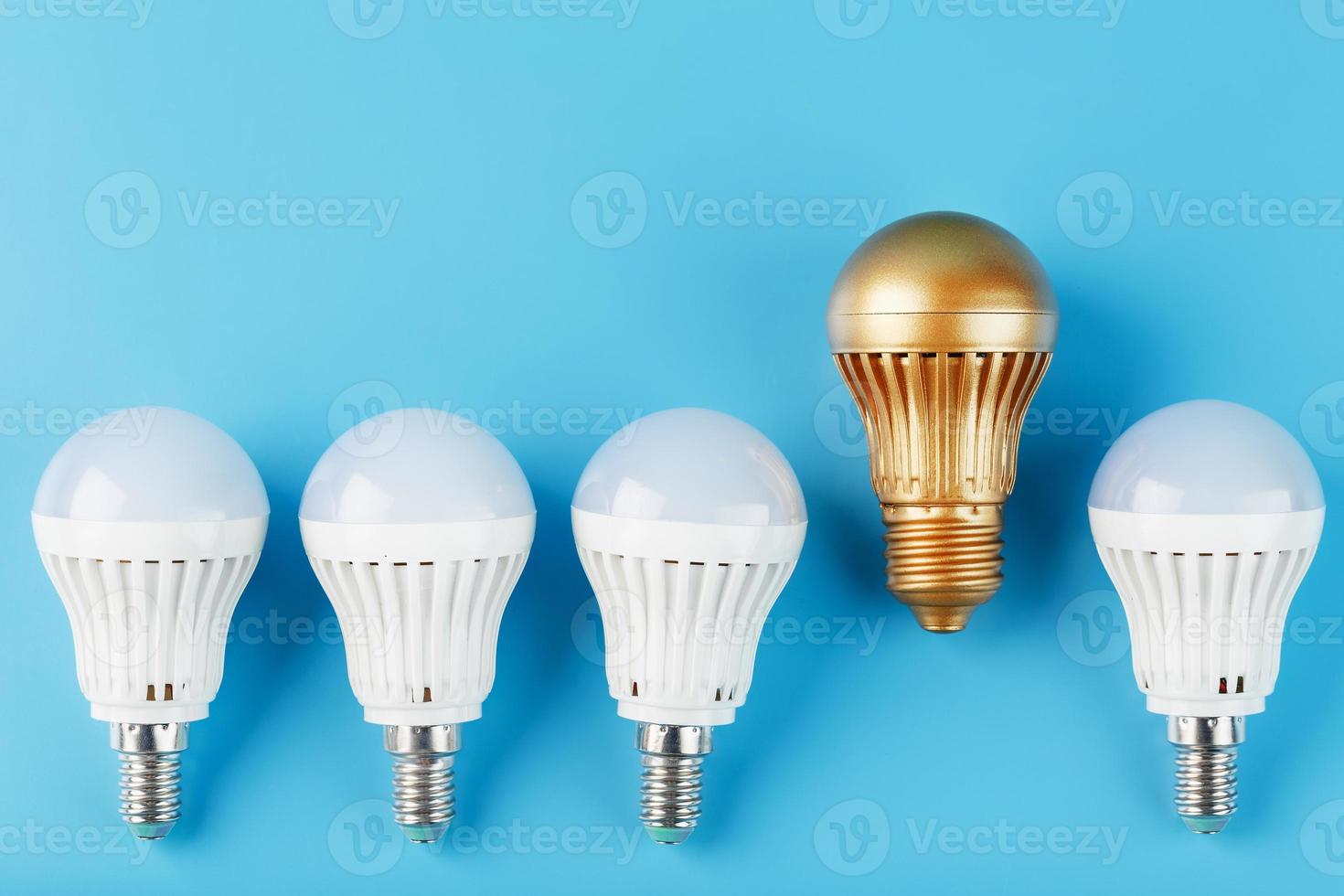 Eine goldene LED-Glühbirne ist höher und hebt sich von einer Reihe weißer Lampen auf blauem Hintergrund ab. foto