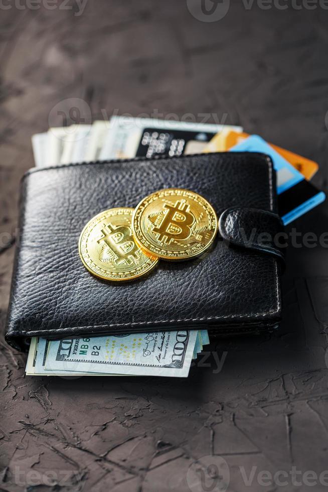 Eine schwarze Brieftasche mit Dollar, E-Cards und Bitcoins auf schwarzem, strukturiertem Hintergrund. foto