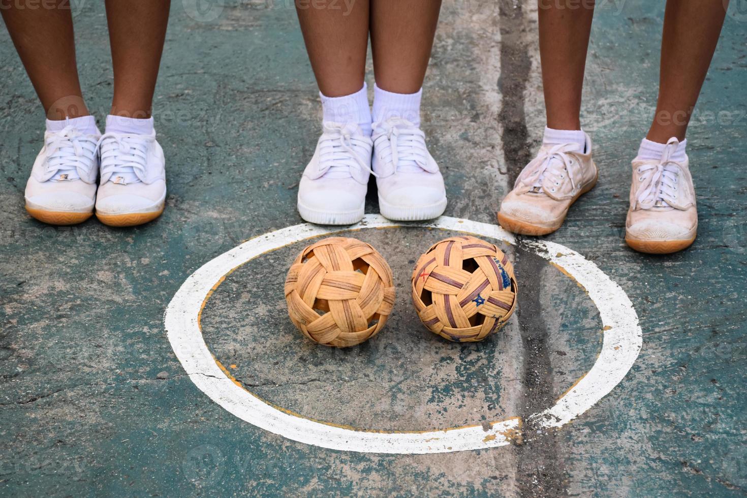 junge südostasiatische sepak-takraw-spielerinnen, die in der nähe der bälle in der umschlagsmitte des platzes stehen, sepak-takraw im freien spielen nach der schule, weicher und selektiver fokus. foto