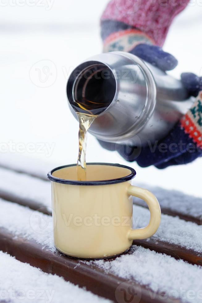 Frau gießt Tee aus Thermoskanne in Tasse auf einem Spaziergang im Winterpark. foto