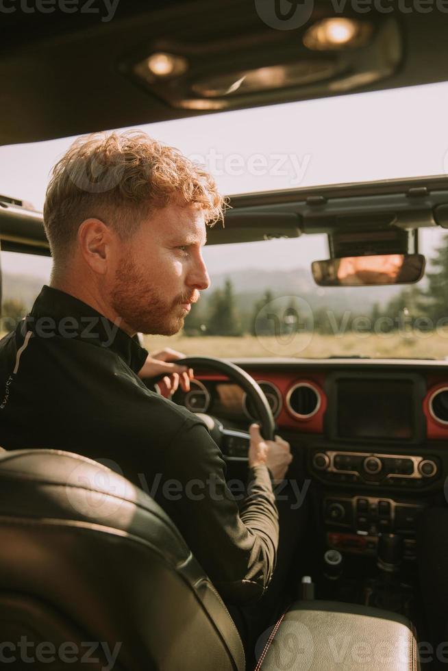 junger Mann mit roten Haaren, der ein Geländefahrzeug auf einem Roadtrip in der Natur fährt foto