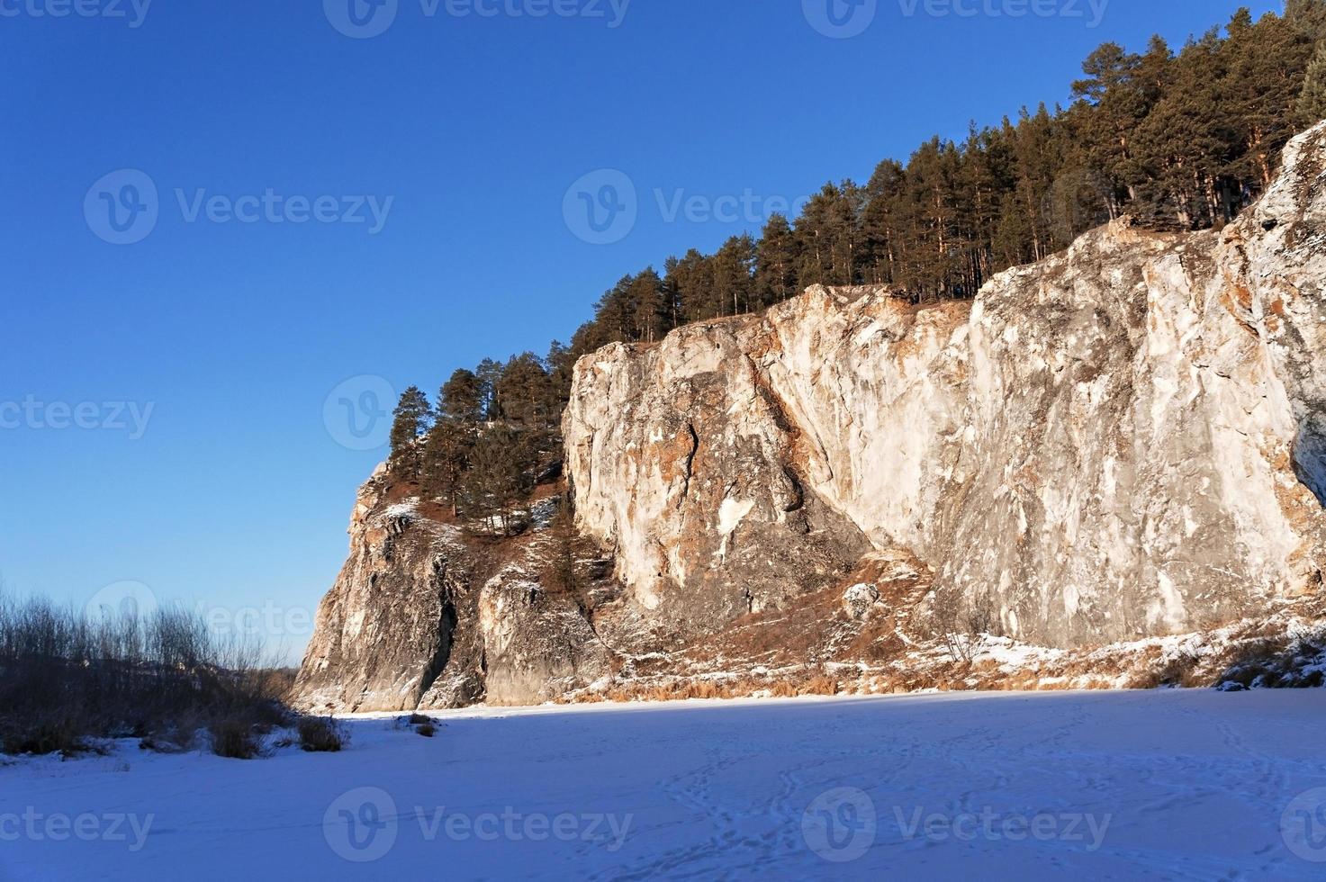 Winterberglandschaft mit Klippen an einem zugefrorenen und schneebedeckten Fluss. Felsen mit Kiefern, malerische Natur foto