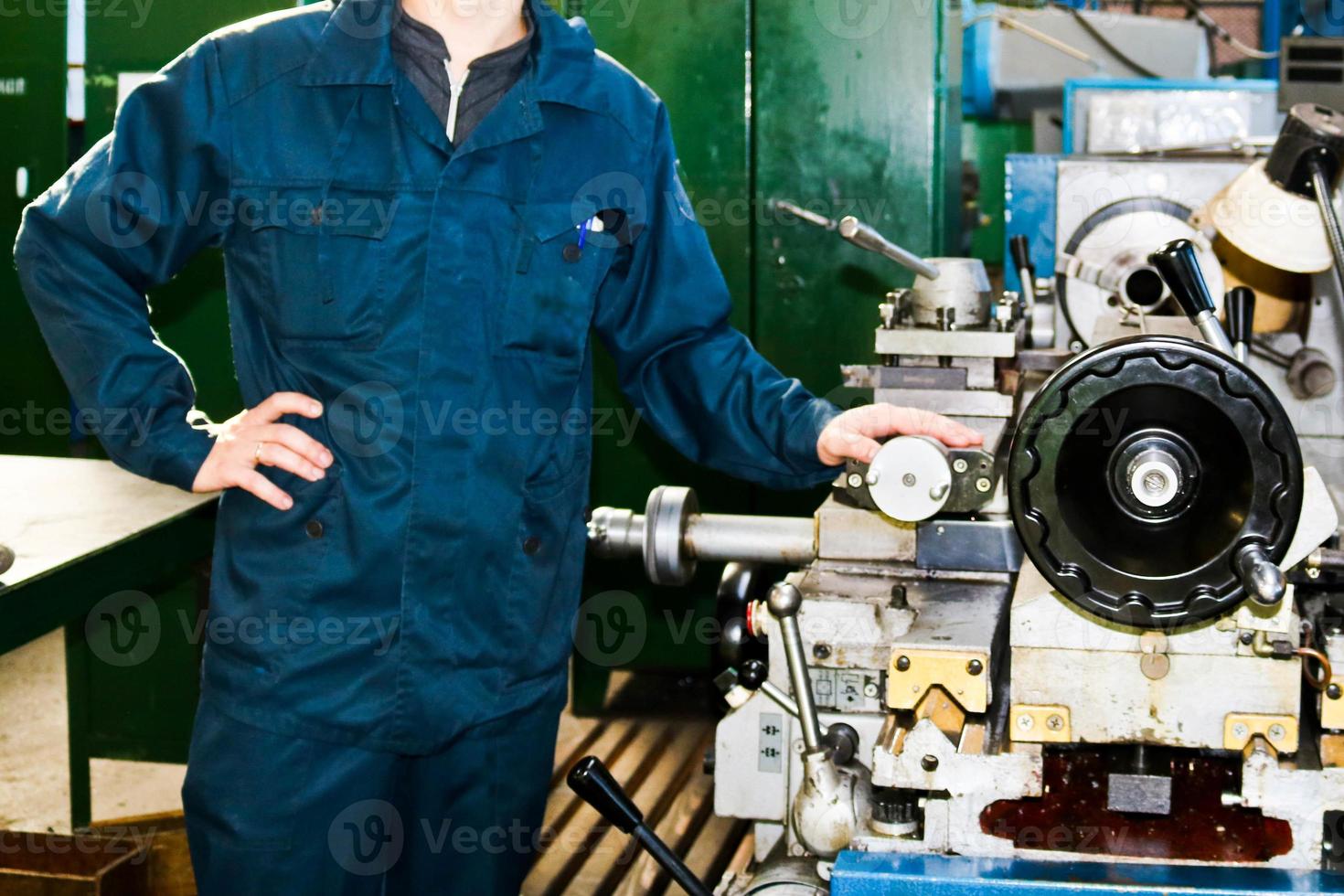 Ein Mann, der in einem Gewand arbeitet, steht neben einer Industriedrehmaschine zum Schneiden, Drehen von Messern aus Metallen, Holz und anderen Materialien, Drehen, Herstellen von Details und Ersatzteilen in der Fabrik foto