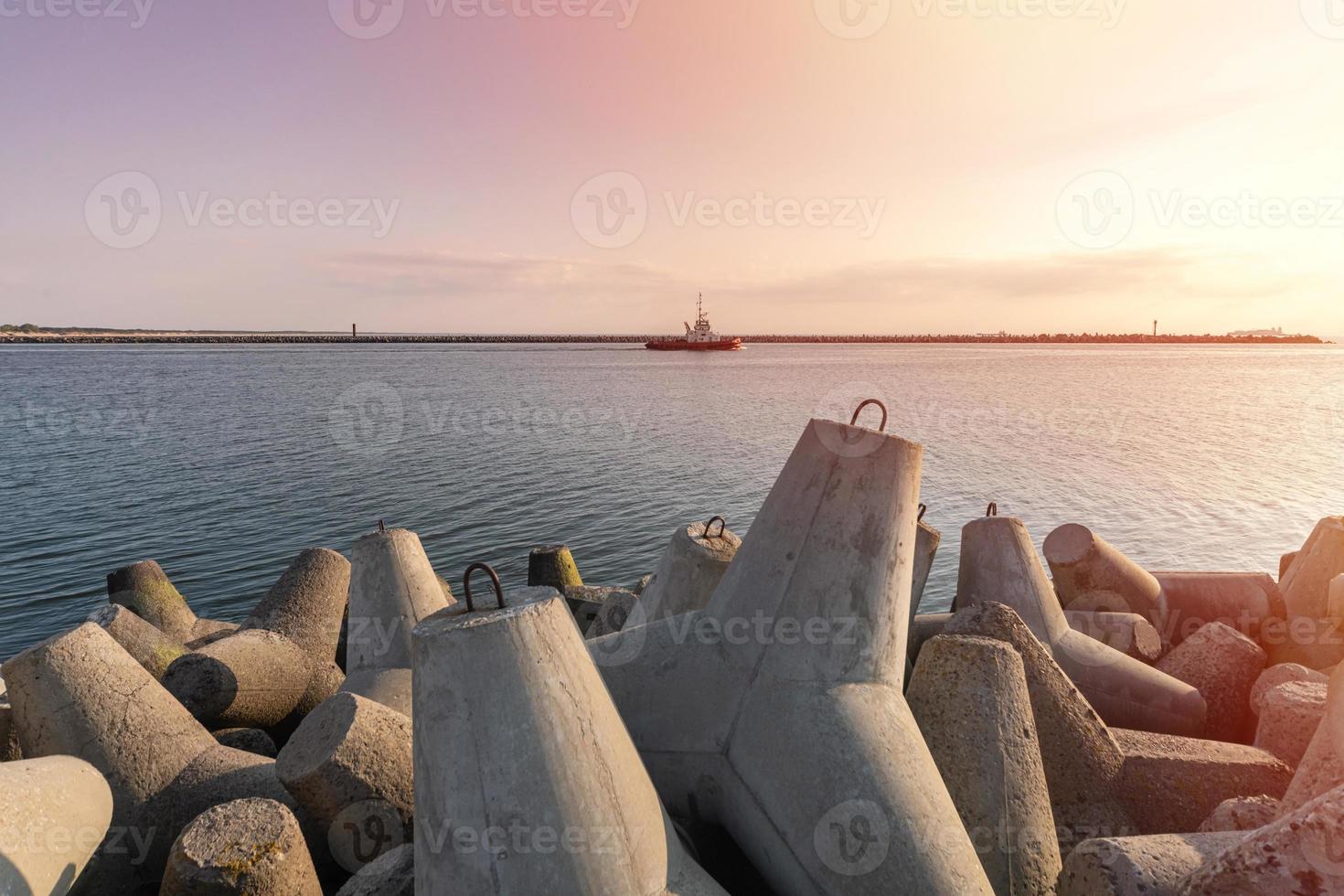 Schlepper, der im Meer segelt, um das Schiff zum Hafen zu schleppen. Tetrapoden-Wellenbrecher im Hafen. schöner Sonnenuntergang über dem Pier. foto