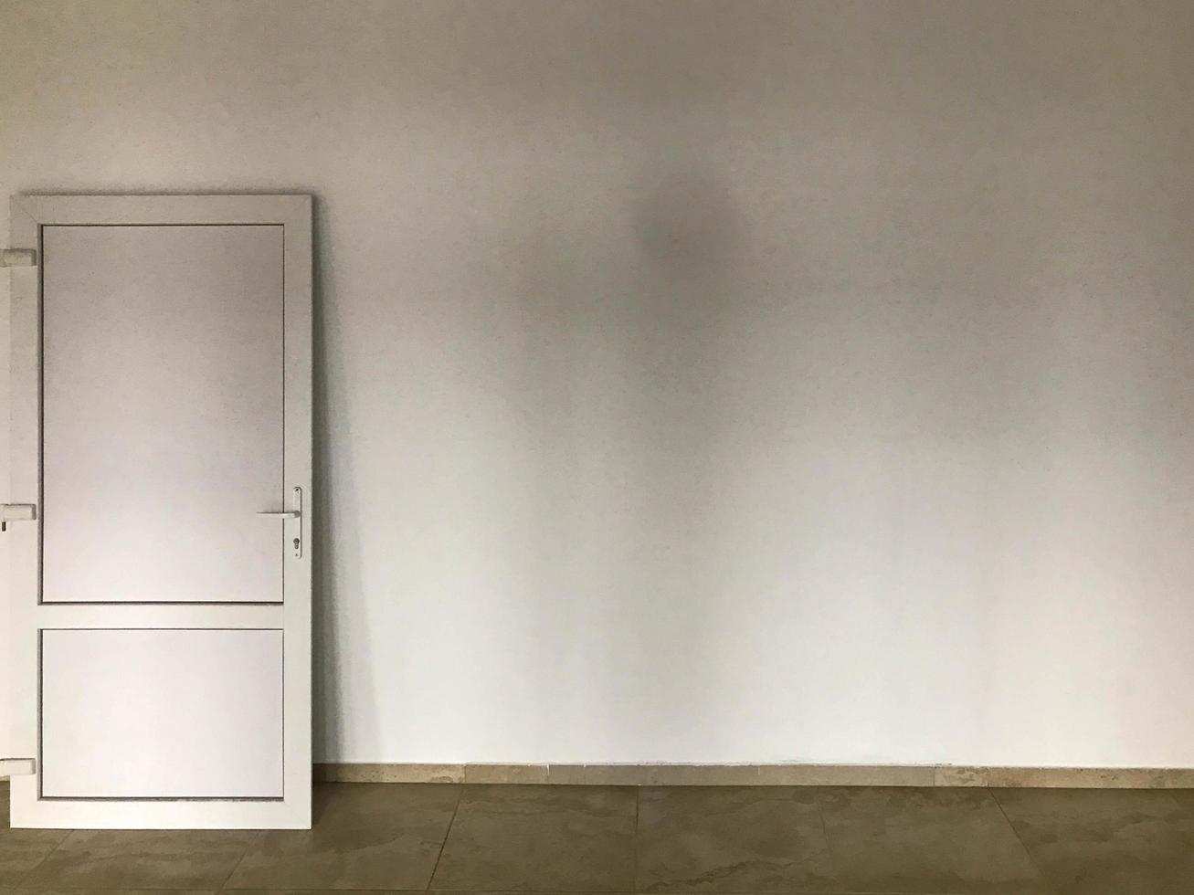 eine weiße kunststofftür steht an einer weiß verputzten wand. Innenrenovierung. Installation von Türen, Außen- und Innendekoration. Reparaturtür auf einem braun gestrichenen Boden foto