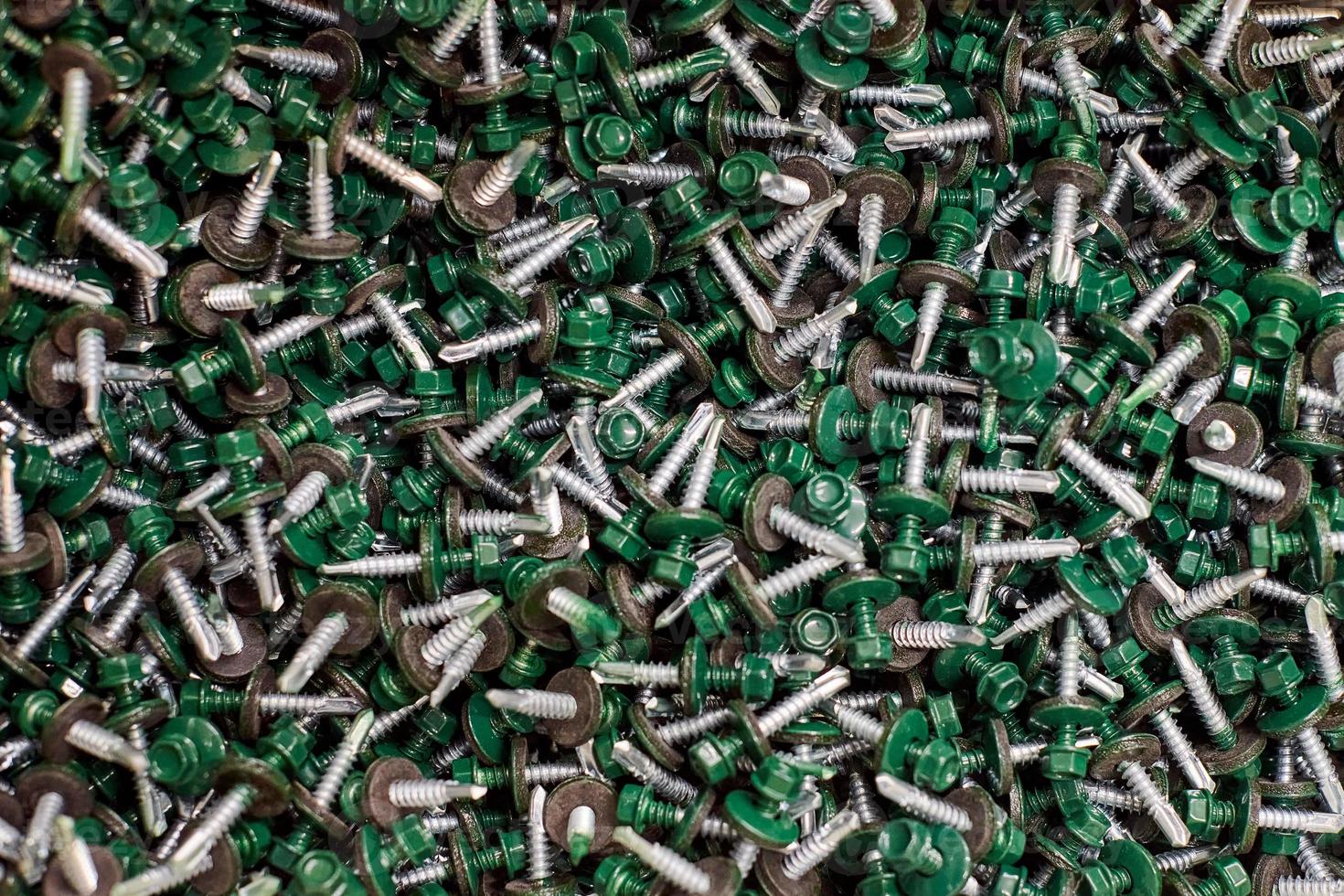 Haufen verzinkter selbstbohrender Schrauben mit Unterlegscheibe und grünem Sechskantkopf, Hardware-Hintergrund foto
