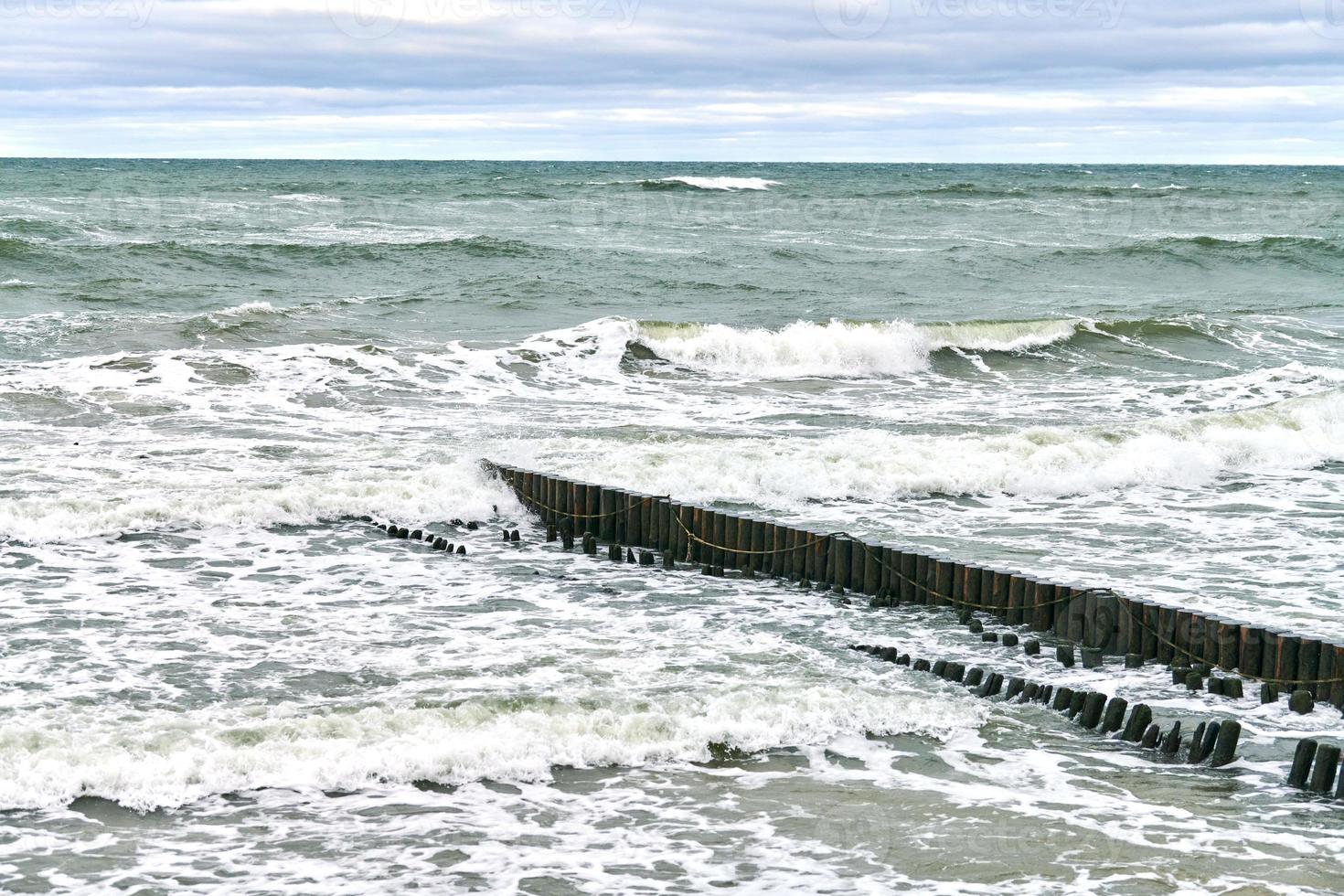 Blick auf das blaue Meer mit schäumenden Wellen und hölzernen Wellenbrechern foto