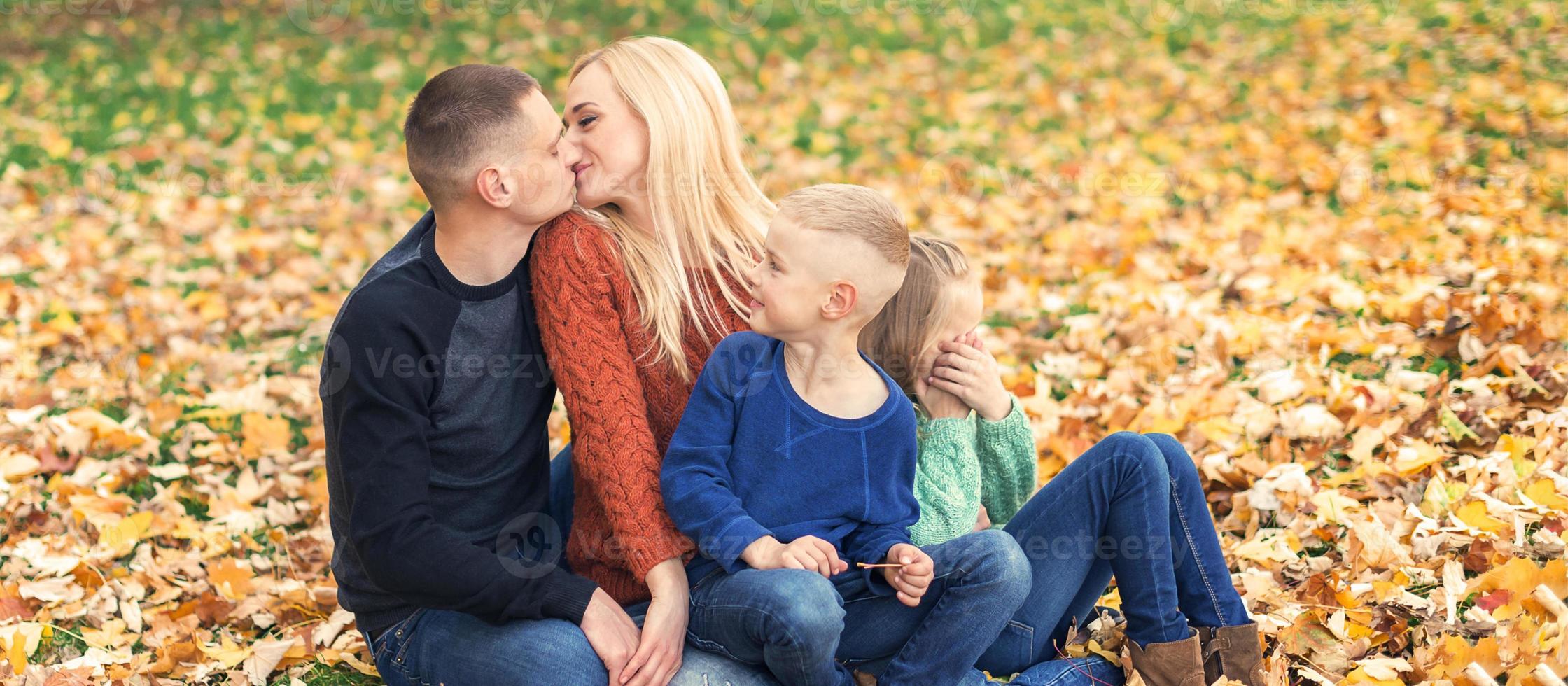 Porträt einer jungen Familie, die im Herbstlaub sitzt foto