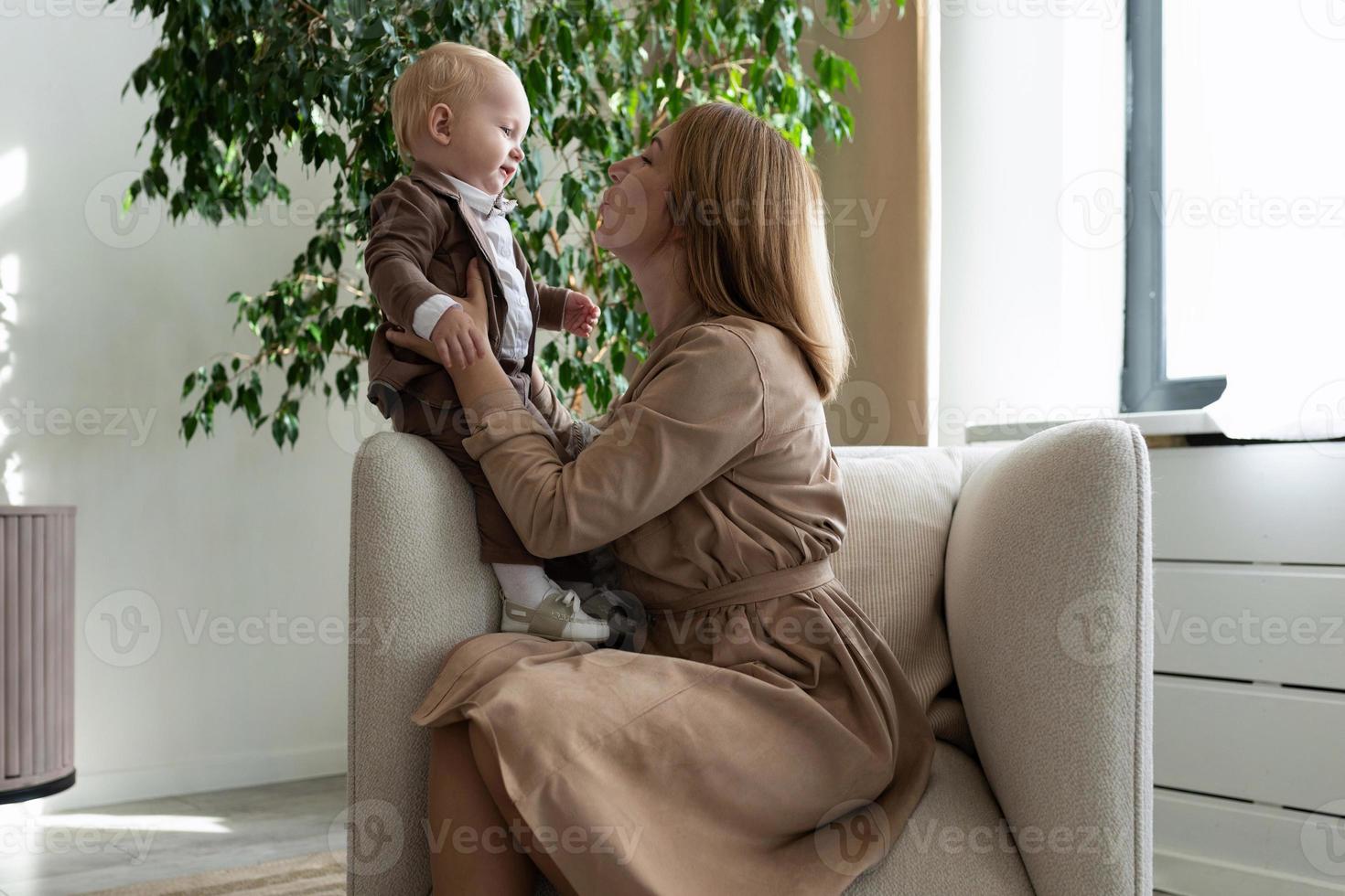 glückliche Mutter mit ihrem kleinen Kind sitzt auf einem Stuhl foto