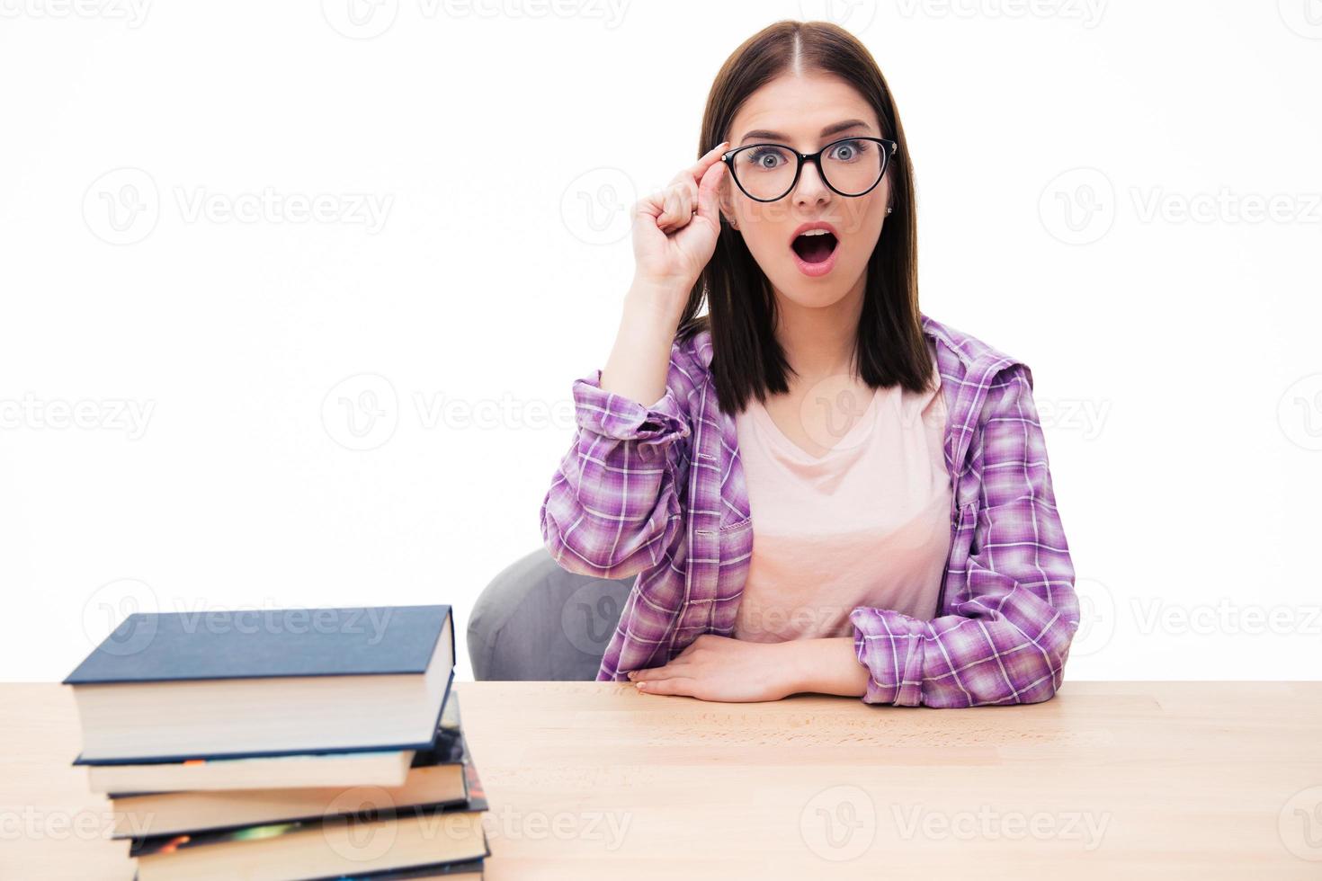 überraschte Frau, die mit Büchern am Tisch sitzt foto