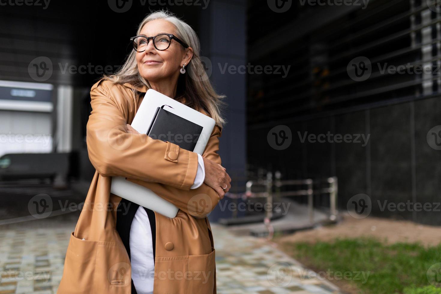 glücklicher älterer geschäftsmann mit einem laptop in seinen händen nahe dem geschäftszentrum foto