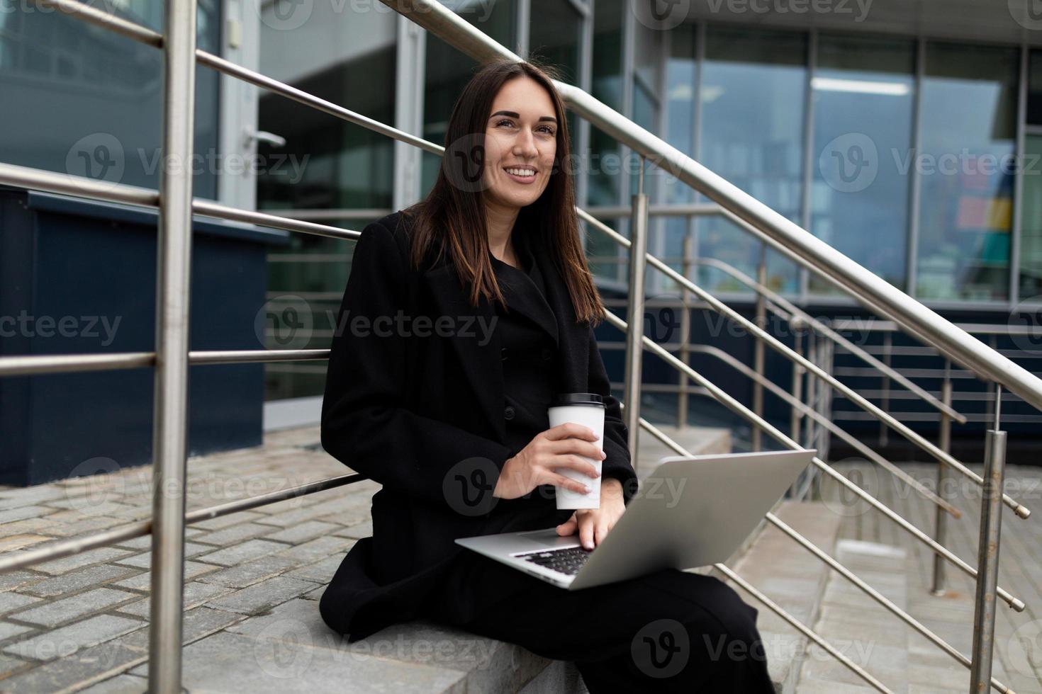 moderne erfolgreiche Geschäftsfrau, die online mit einem Lächeln auf ihrem Gesicht am Laptop arbeitet foto