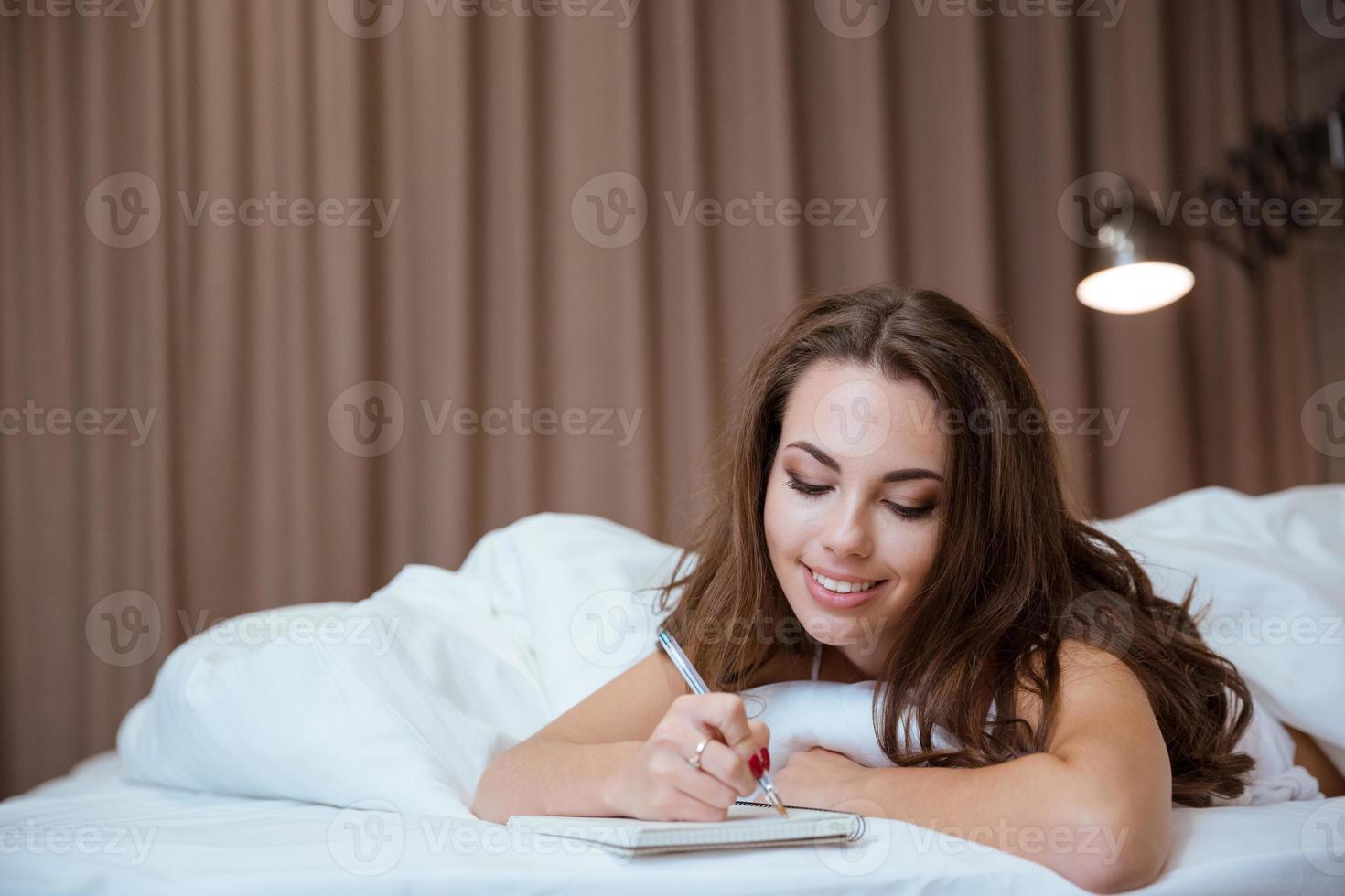 Frau, die Notizen im Notizblock macht, während sie auf dem Bett liegt foto