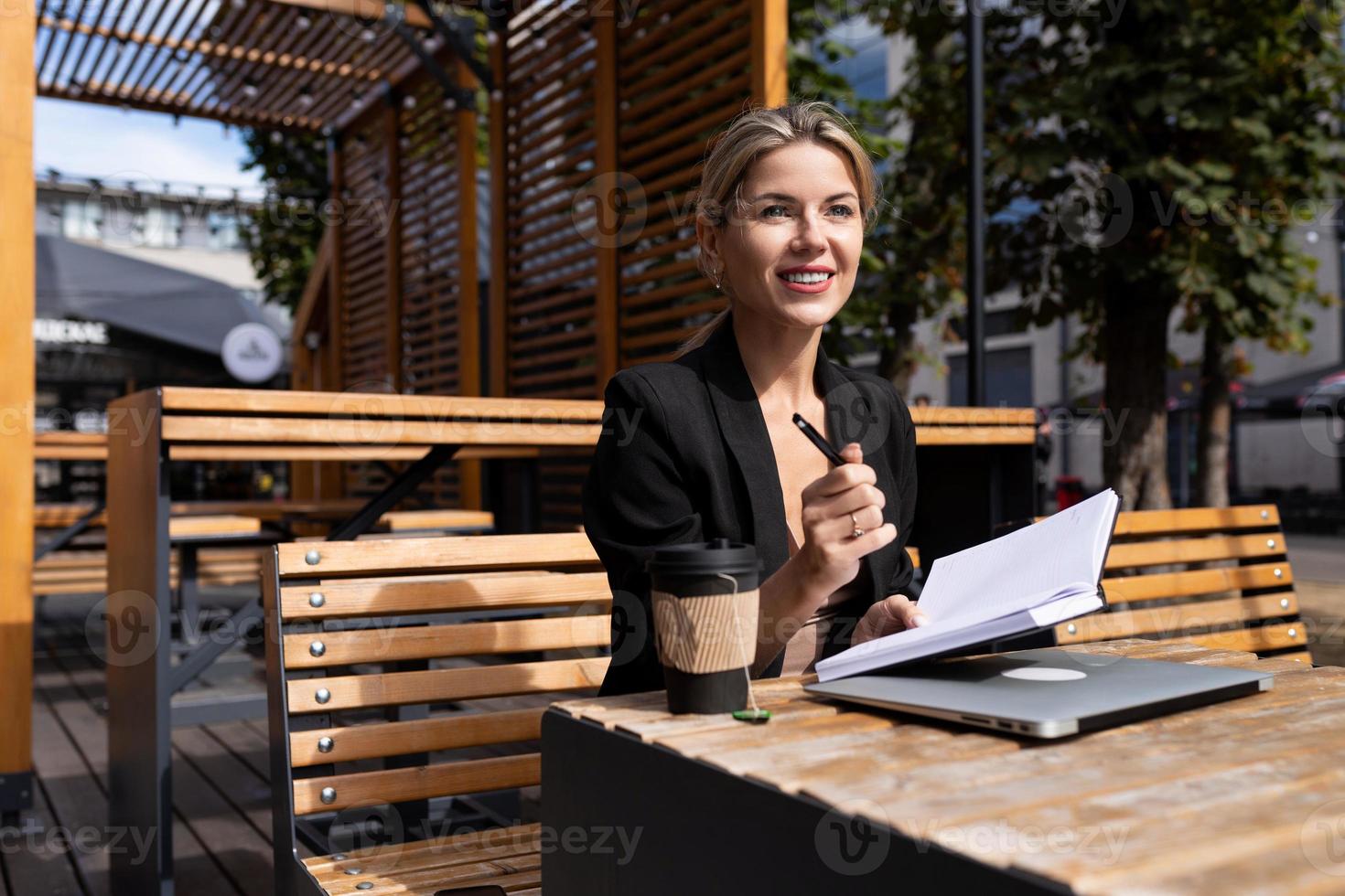 Spezialistin für junge Frauen arbeitet im Freien mit einem Laptop und macht sich Notizen in einem Tagebuch foto
