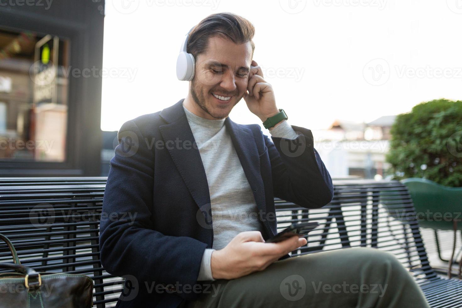 ein junger mann hört gerne musik über kopfhörer und sieht ein handy mit einem breiten lächeln im gesicht an, konzept eines remote-videokonferenztreffens foto