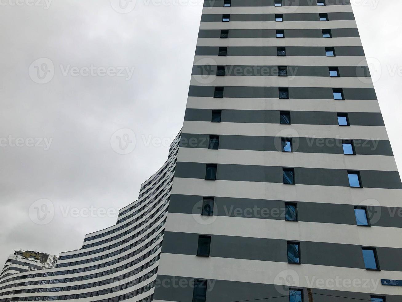 hohes Wohngebäude, Wolkenkratzer in Form einer Welle. von der Seite ist das Haus blau und weiß. viele kleine Glasfenster um den Umfang. Wolkenkratzer auf dem Hintergrund des bewölkten Himmels foto