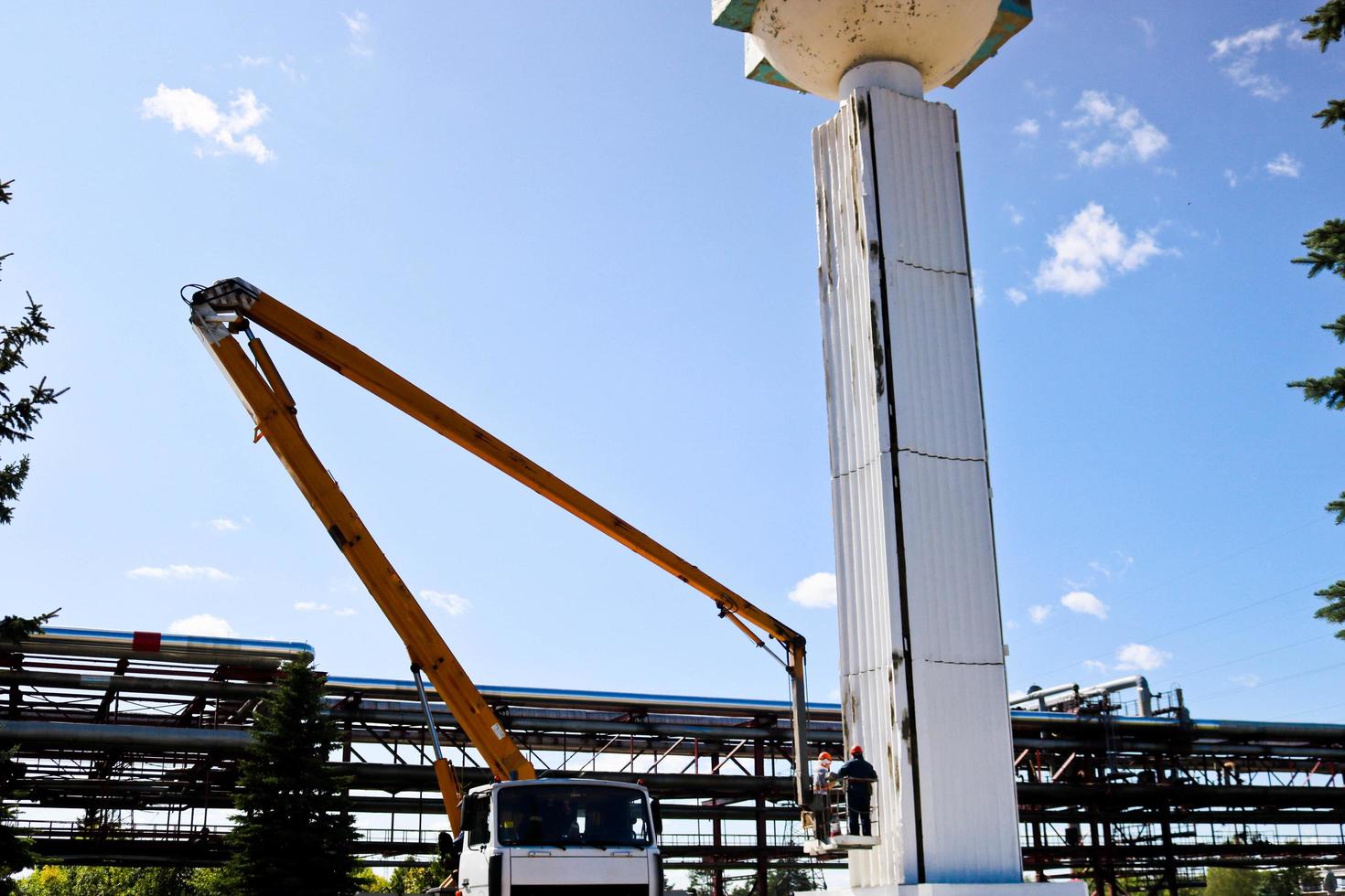 Spalten mit einer speziellen Technik reparieren. Arbeiter am Kran reparieren eine große weiße Säule. Schönheitsreparatur mit Lackierung. Arbeiter in Sonderform bemalen eine Säule foto