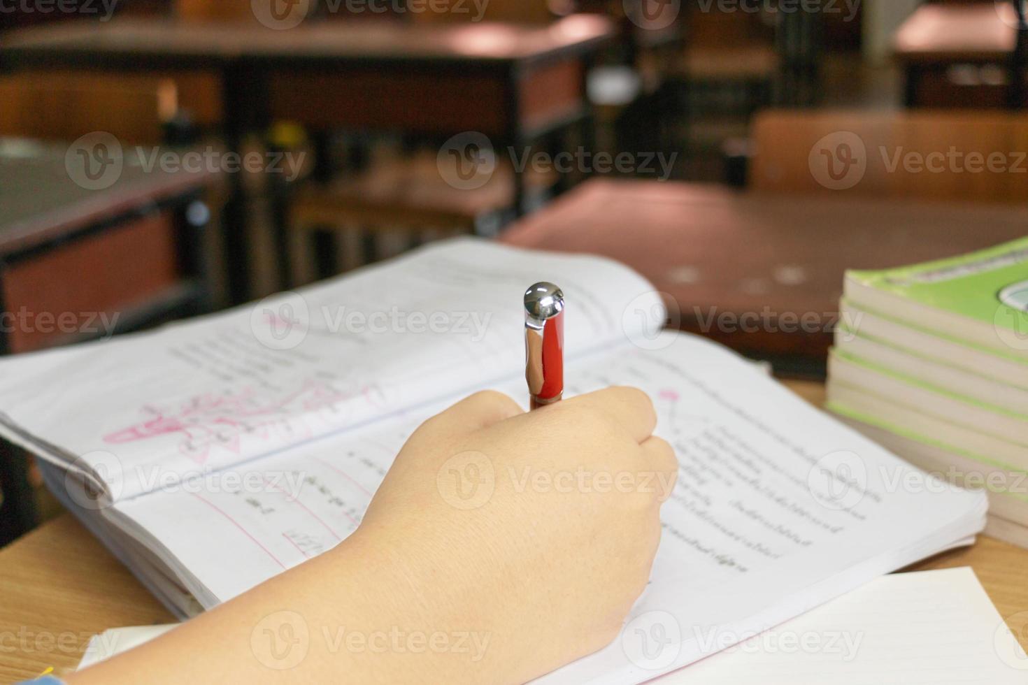 Die Hand des Lehrers hält einen roten Stift, der die Hausaufgaben des Schülers überprüft foto