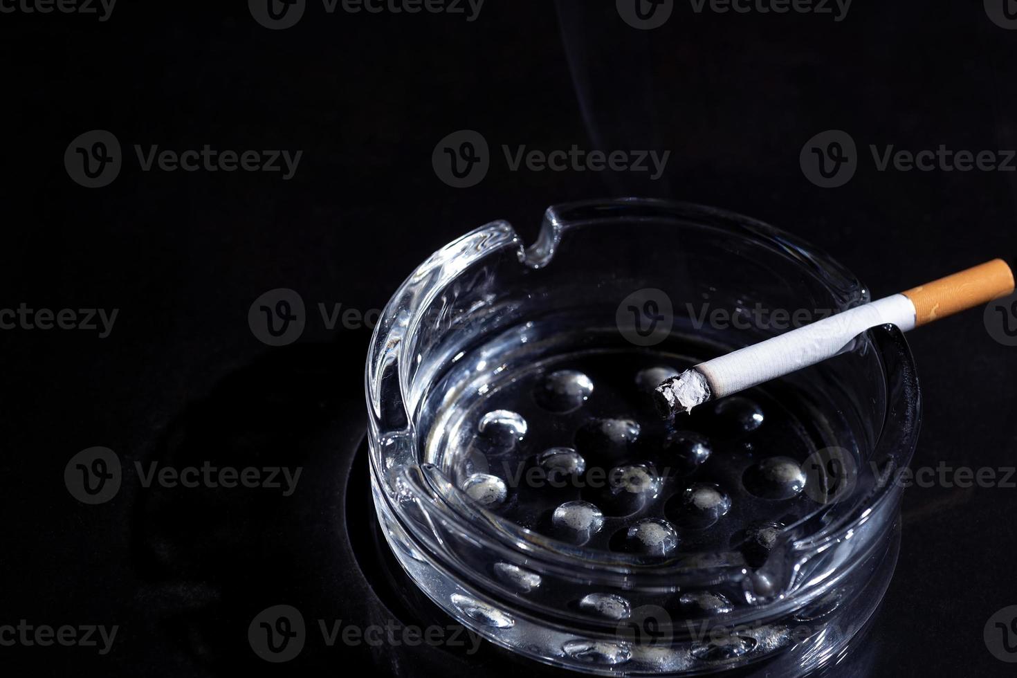 Aschenbecher und rauchende Zigarette auf schwarzem Hintergrund foto