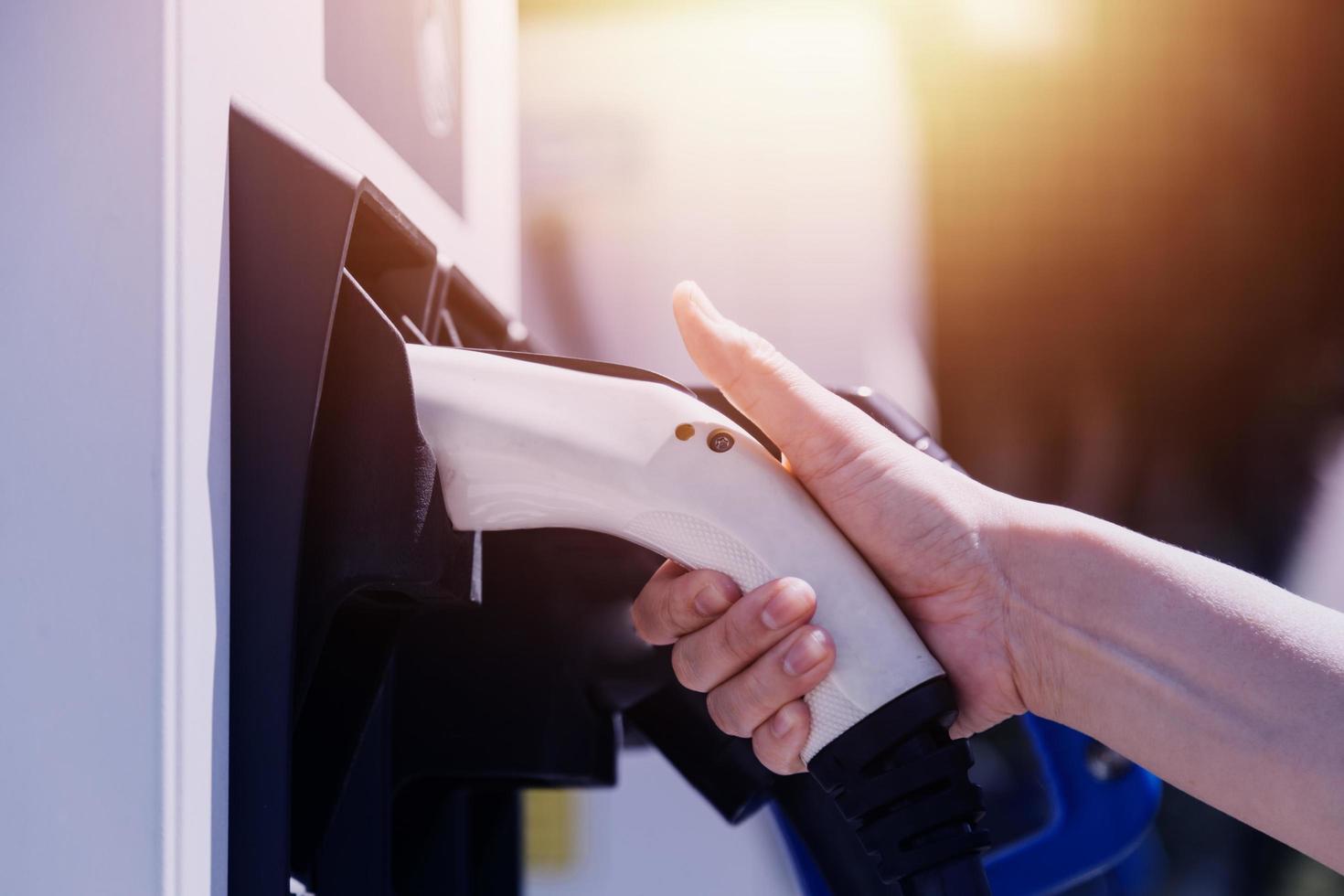 hand, die ein ladegerät in eine elektroautosteckdose einsteckt. elektroauto oder ev wird an der station aufgeladen foto