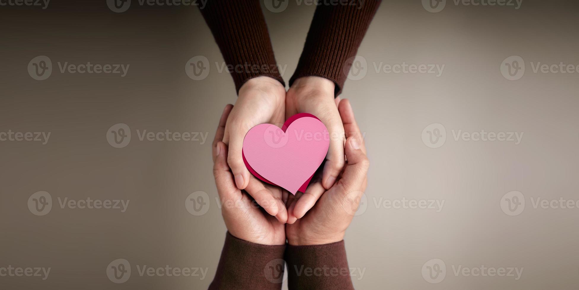 Liebes- und Beziehungskonzepte. Hände eines Paares, das zusammen Herzformpapier umarmt. Valentinstag. Schutz der Liebe und Familie durch sanfte Hand. Ansicht von oben foto