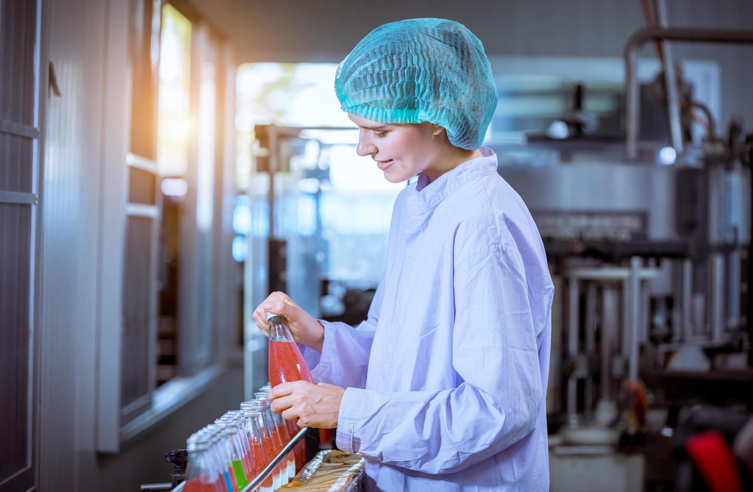 arbeiter der wissenschaft in der flaschengetränkefabrik mit sicherheitshut, der vor der verteilung an das marktgeschäft die qualität der basilikumsamenprodukte auf dem förderband überprüft. foto