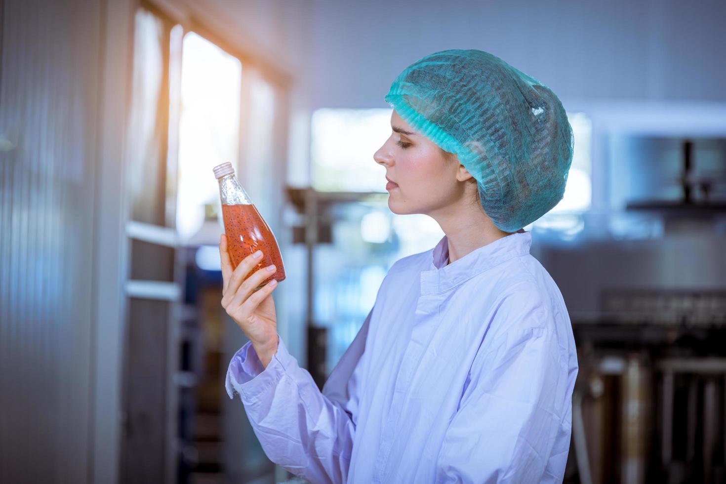 arbeiter der wissenschaft in der flaschengetränkefabrik mit sicherheitshut, der vor der verteilung an das marktgeschäft die qualität der basilikumsamenprodukte auf dem förderband überprüft. foto