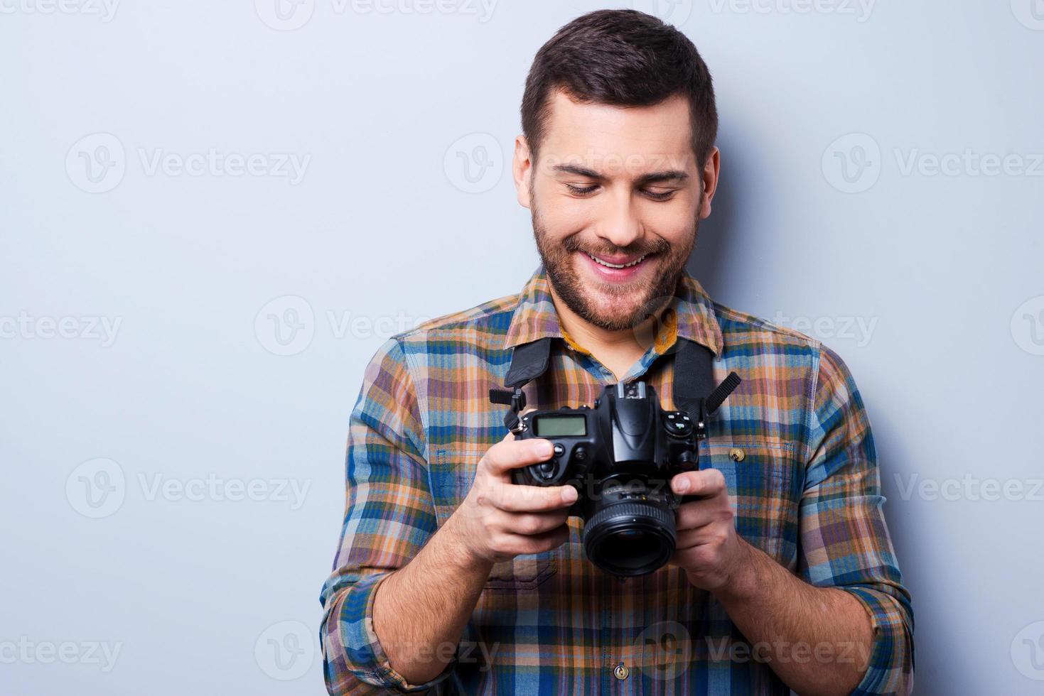 Einstellung der Kamera. Porträt eines selbstbewussten jungen Mannes im Hemd, der die Kamera hält, während er vor grauem Hintergrund steht foto