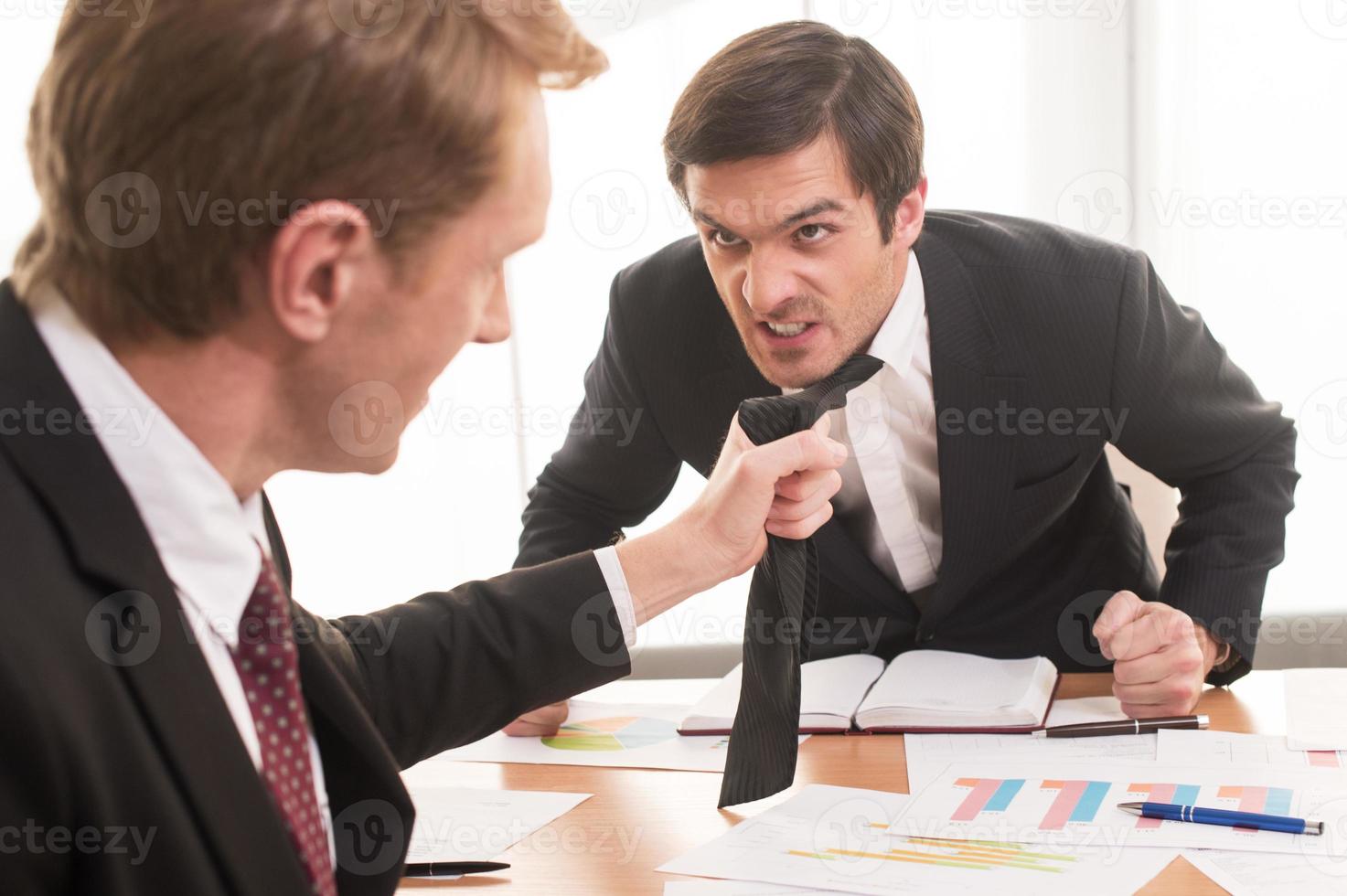 Konflikte am Arbeitsplatz. Zwei junge Männer in festlicher Kleidung streiten sich, während einer von ihnen die Krawatte seines Gegners ergreift foto