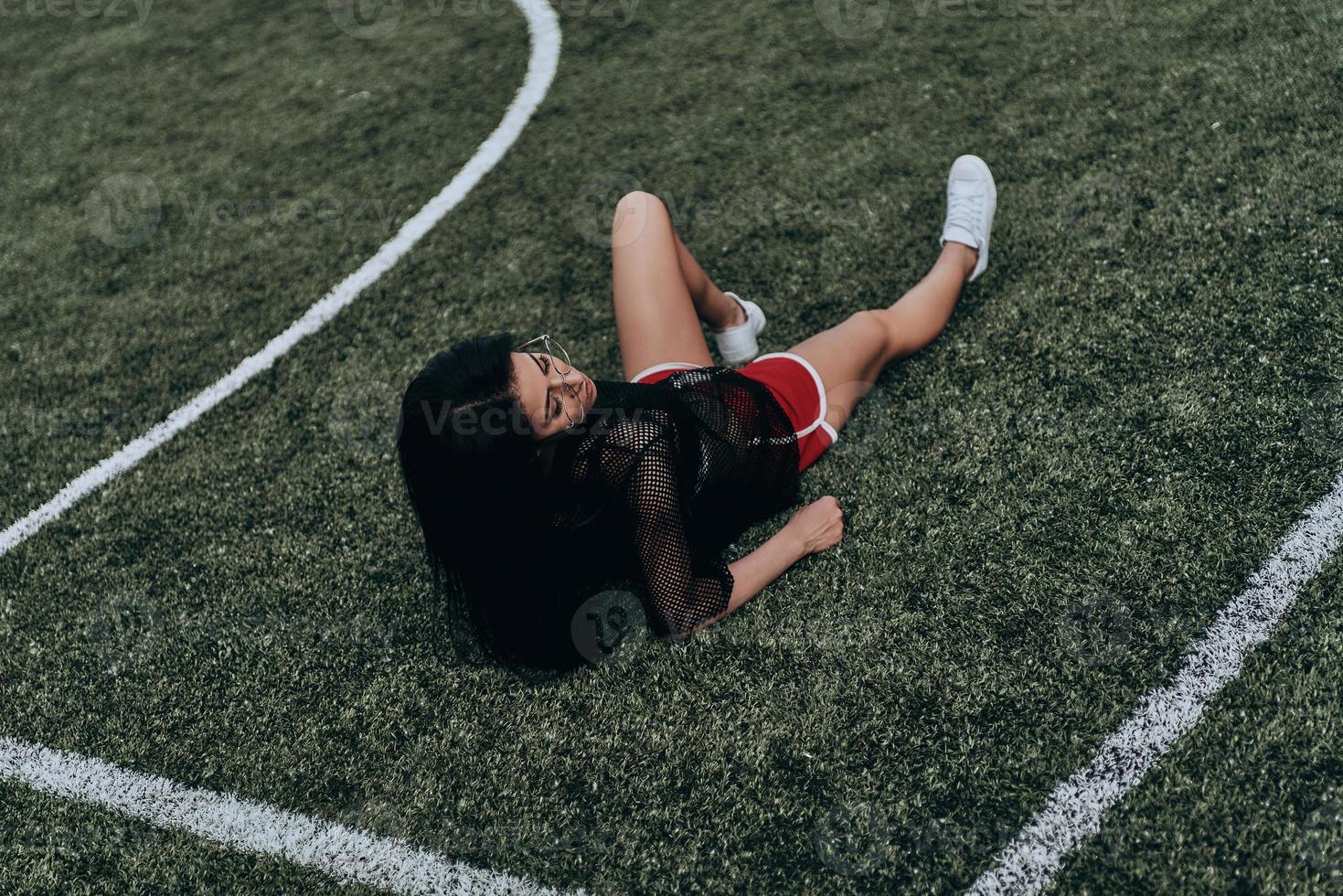 einfach sie selbst sein. Schöne junge Frau in Sportkleidung, die die Augen geschlossen hält, während sie auf dem Fußballplatz liegt foto