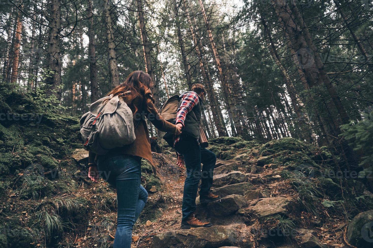 keine Zeit zum Entspannen. Rückansicht eines modernen jungen Paares, das Händchen hält und sich beim gemeinsamen Wandern im Wald nach oben bewegt foto