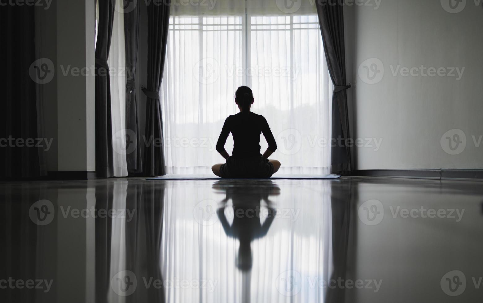 Silhouette einer jungen Frau, die zu Hause meditiert. männer, die drinnen yoga praktizieren. entspannung, körperpflege, meditation, balance, fitness, training, erholungskonzept, beten. foto