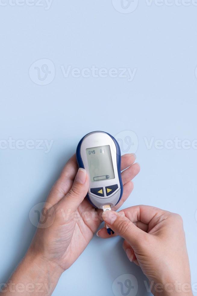Draufsicht der weiblichen Hände mit Glukosemeter auf blauem Hintergrund. Krankheit Diabetes-Konzept foto
