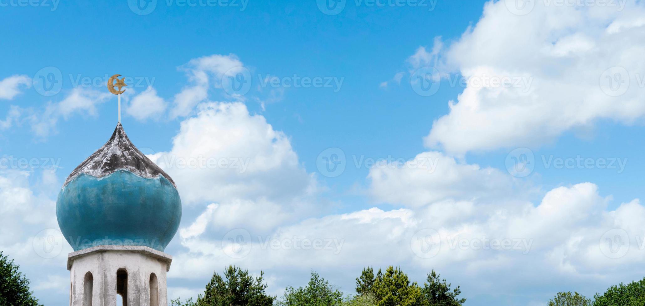 Halbmond und Stern auf der Spitze der Moschee über den Wolken auf blauem Himmel und grünem Waldbaumhintergrund. die moschee ist wichtig für die islamische religion, eid al-adha, eid mubarak, eid al fitr, ramadan kareem foto