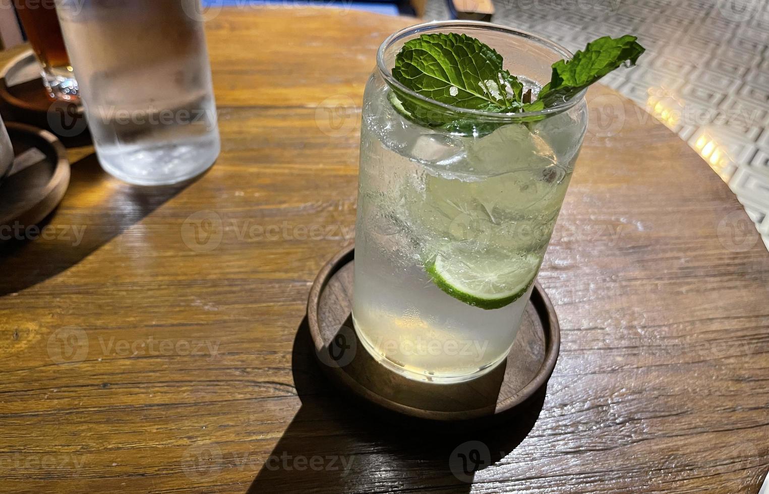 selektiver fokus, köstlicher erfrischender sommermojito mit eis, limette und minze in einem glas mit grops. Holzhintergrund foto