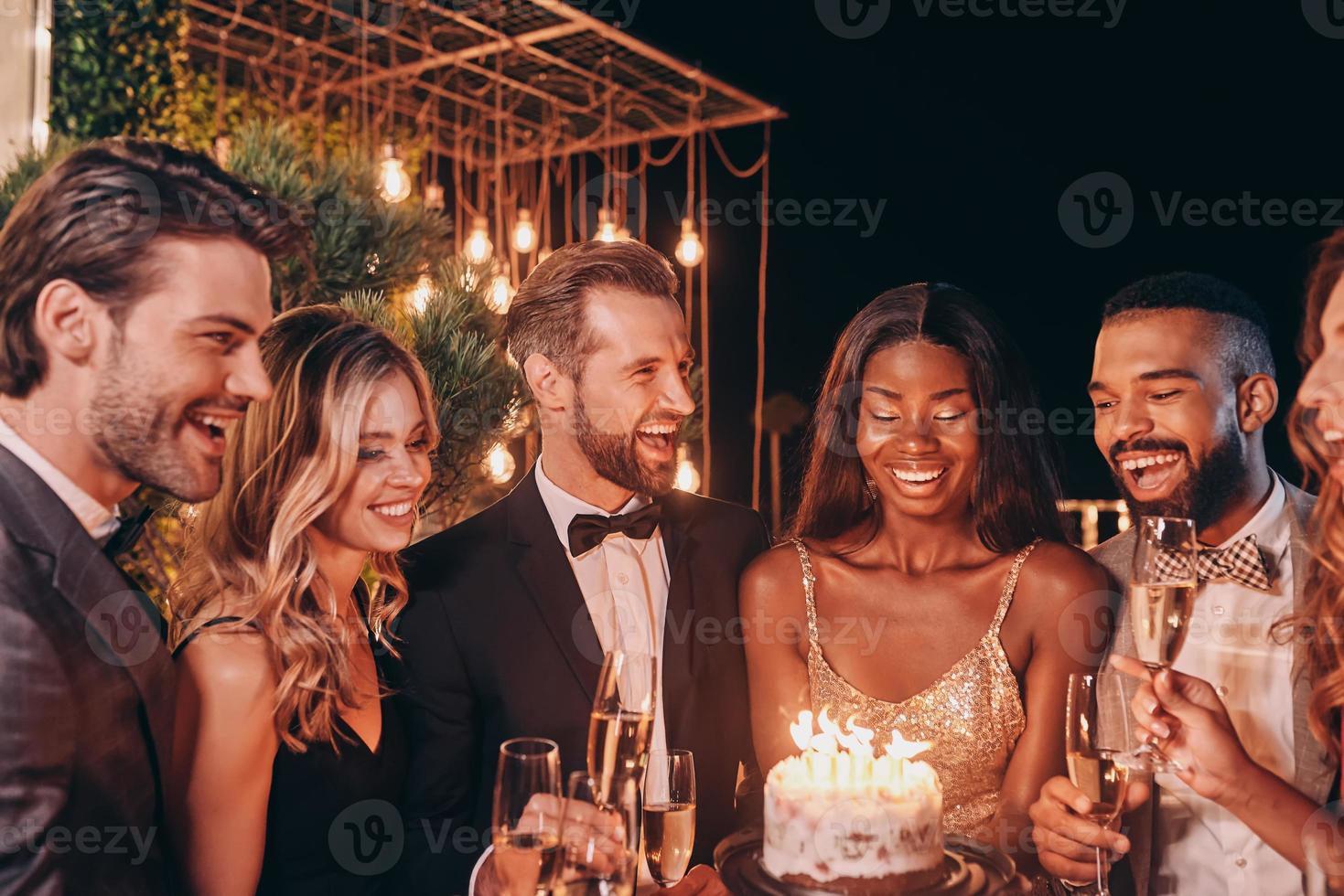 gruppe von menschen in formaler kleidung, die geburtstagstorte halten, während sie zeit auf der party verbringen foto