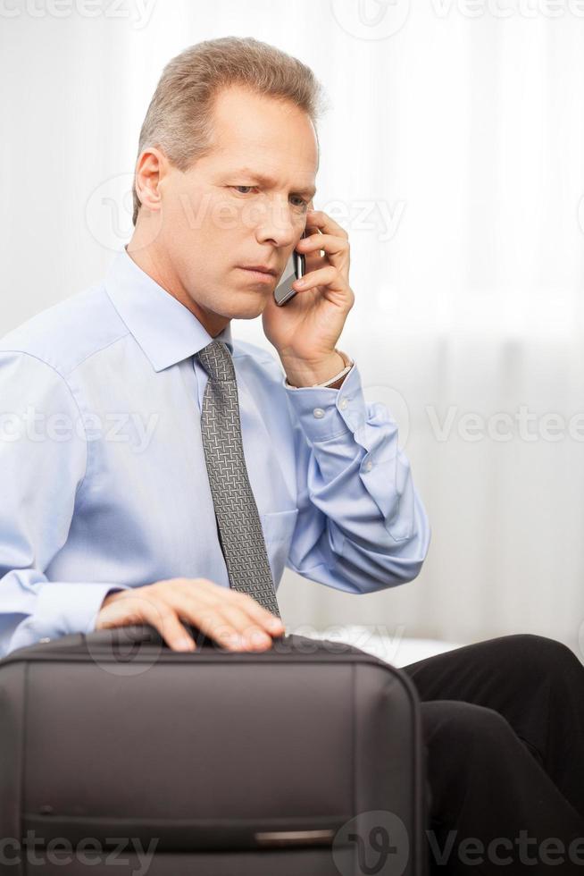 selbstbewusste Führungskraft. ernsthafter Mann mit grauen Haaren in Hemd und Krawatte, der am Telefon spricht, während er auf dem Bett sitzt foto