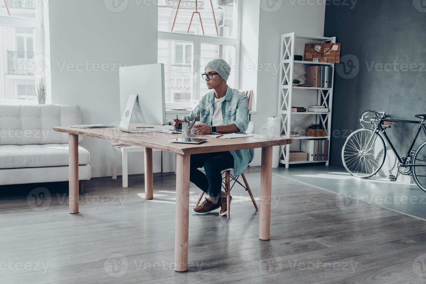 Ideen in etwas Reales umsetzen. hübscher junger Mann in Brillen, der auf den Monitor schaut, während er an seinem Arbeitsplatz im Kreativbüro sitzt foto