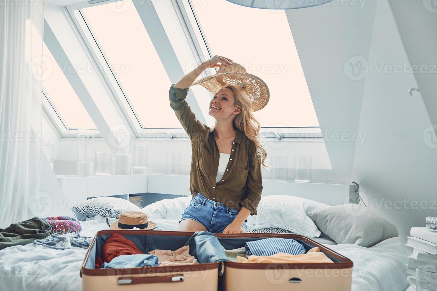 schöne junge lächelnde frau, die gepäck packt, während sie zu hause im bett sitzt foto