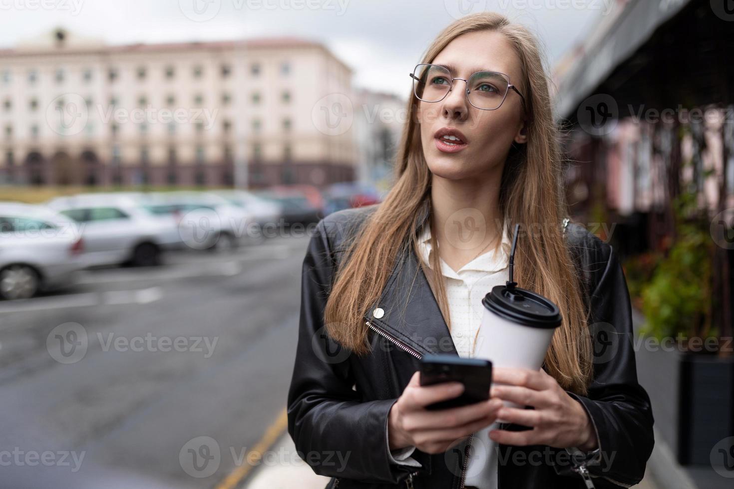 Ein junges Mädchen mit einem Handy in der Hand und einem Glas Kaffee sucht einen Weg in der Stadt foto