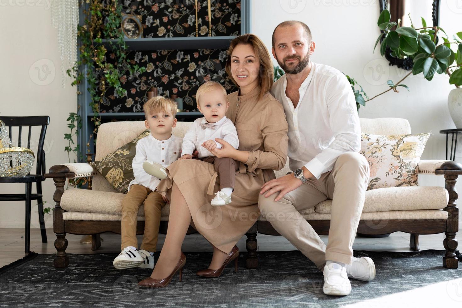 glückliche familie von mama papa und 2 kleinen söhnen, die in beigen kleidern auf dem sofa sitzen foto